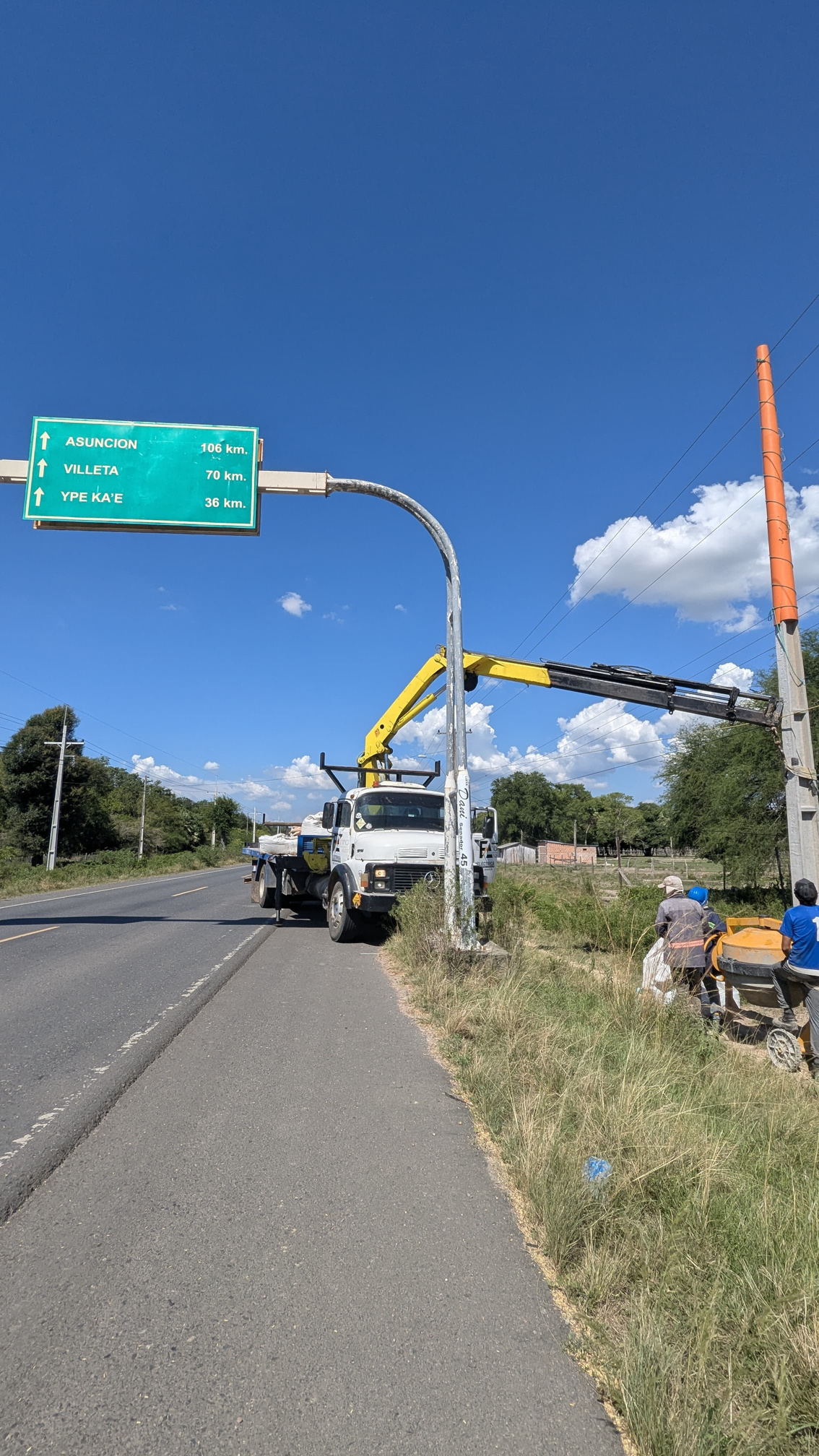 Camión grúa junto a poste eléctrico al borde de una ruta durante un montaje